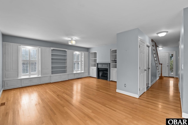 unfurnished living room featuring built in shelves, a fireplace, visible vents, light wood-style floors, and baseboards