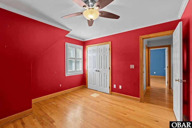 unfurnished bedroom with a closet, ornamental molding, ceiling fan, light wood-type flooring, and baseboards