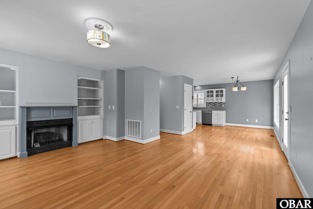 unfurnished living room featuring built in features, a fireplace, visible vents, light wood-style floors, and baseboards