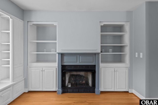 unfurnished living room with built in features, baseboards, a fireplace, and light wood finished floors