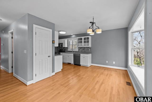 kitchen featuring light wood finished floors, dishwashing machine, backsplash, white cabinetry, and a sink