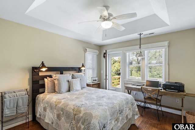 bedroom with a ceiling fan, a tray ceiling, visible vents, baseboards, and dark wood-style floors