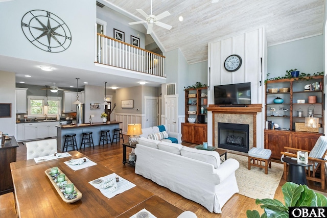 living area featuring a ceiling fan, high vaulted ceiling, a wainscoted wall, wood finished floors, and a fireplace