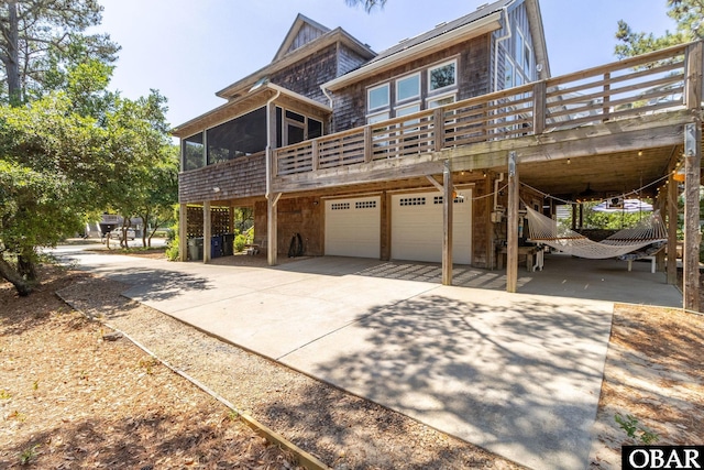 view of front of home featuring a wooden deck, concrete driveway, a garage, and a sunroom