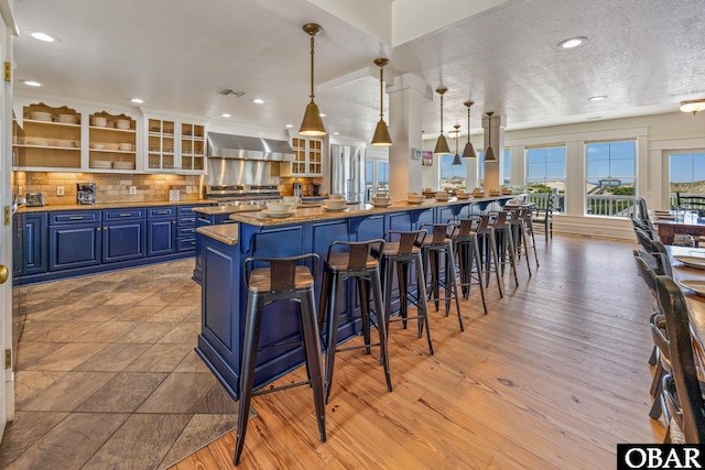 1459 Ocean Pearl Rd Lot 2, 3A, 3B, Corolla, NC 27927 - kitchen with blue cabinets, wall chimney range hood, a breakfast bar, decorative backsplash, and glass insert cabinets