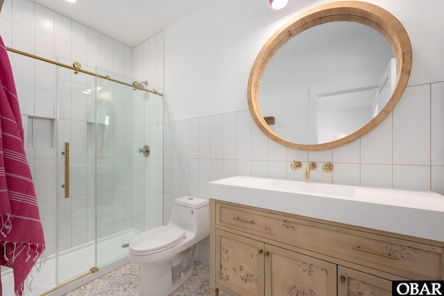 bathroom with toilet, tile walls, a stall shower, and vanity