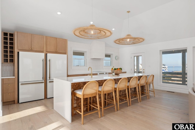 kitchen with light countertops, light wood-type flooring, lofted ceiling, high end fridge, and a sink