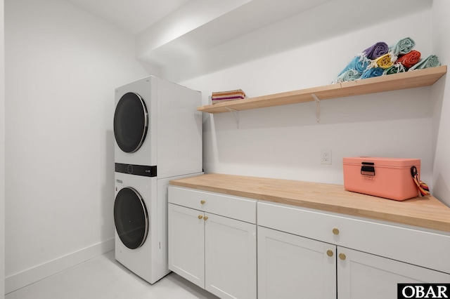 clothes washing area with cabinet space, stacked washer / drying machine, and baseboards