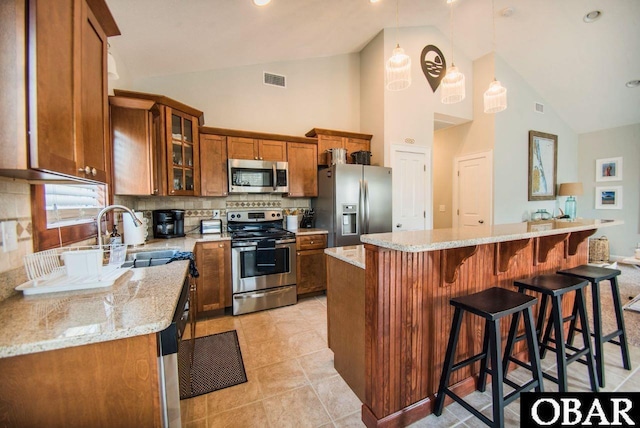 kitchen featuring a breakfast bar area, stainless steel appliances, a kitchen island, brown cabinets, and glass insert cabinets