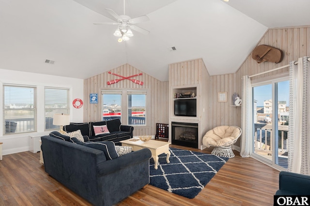 living room with lofted ceiling, wooden walls, a large fireplace, wood finished floors, and visible vents