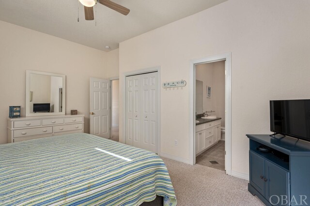 bedroom with a closet, ensuite bathroom, light carpet, a sink, and baseboards