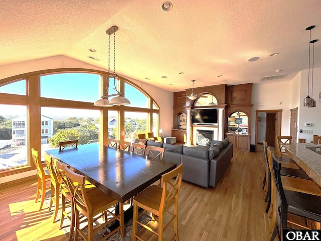 dining room featuring a textured ceiling, visible vents, light wood-style floors, vaulted ceiling, and a glass covered fireplace