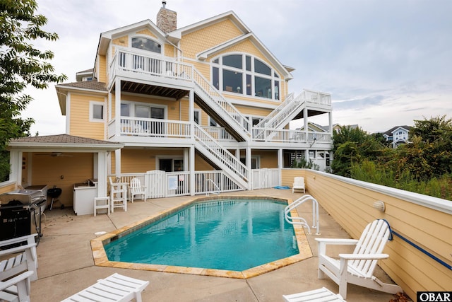 rear view of property with an outdoor pool, a balcony, a chimney, stairs, and a patio area