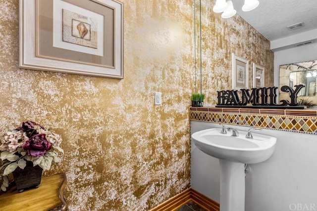 bathroom with visible vents, a textured ceiling, baseboards, and wallpapered walls