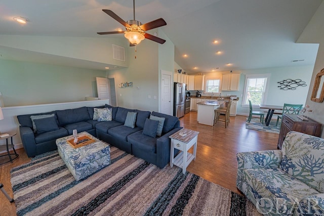 living area featuring high vaulted ceiling, visible vents, baseboards, and wood finished floors