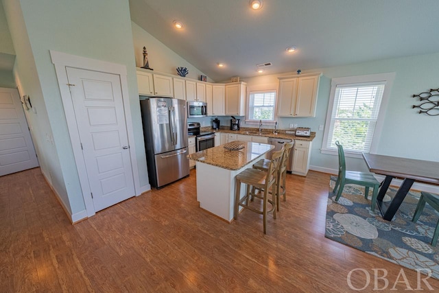 kitchen featuring lofted ceiling, stainless steel appliances, a breakfast bar, a sink, and a kitchen island