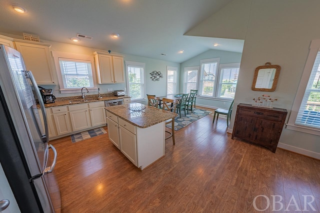 kitchen featuring a center island, stainless steel appliances, a sink, wood finished floors, and a kitchen breakfast bar