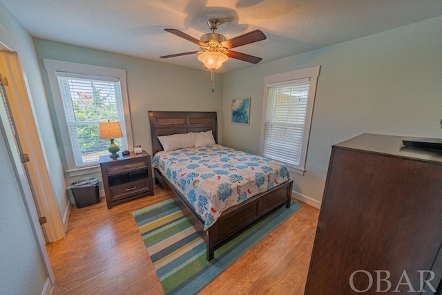 bedroom featuring light wood-type flooring, ceiling fan, baseboards, and a textured ceiling