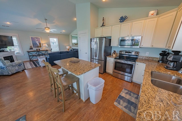 kitchen featuring stainless steel appliances, a sink, a center island, open floor plan, and light stone countertops