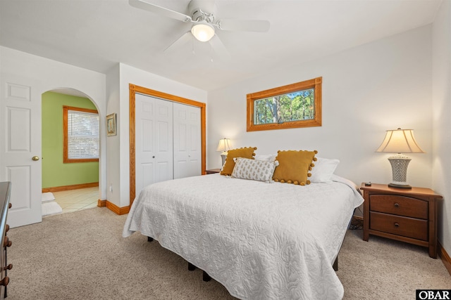 bedroom with arched walkways, ceiling fan, light carpet, baseboards, and a closet