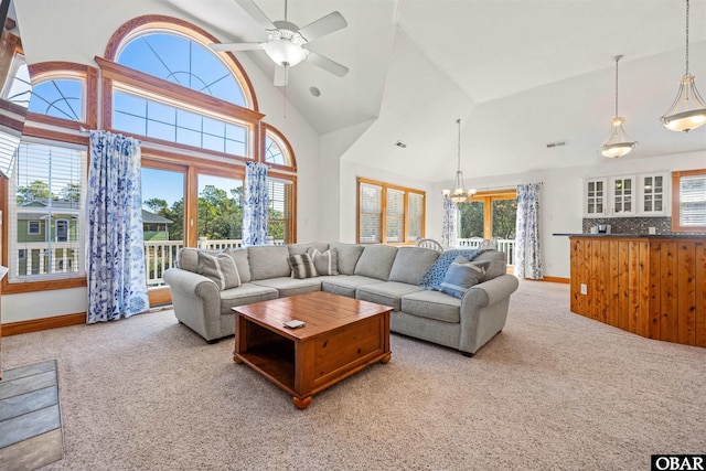 living room with ceiling fan with notable chandelier, high vaulted ceiling, baseboards, and light colored carpet