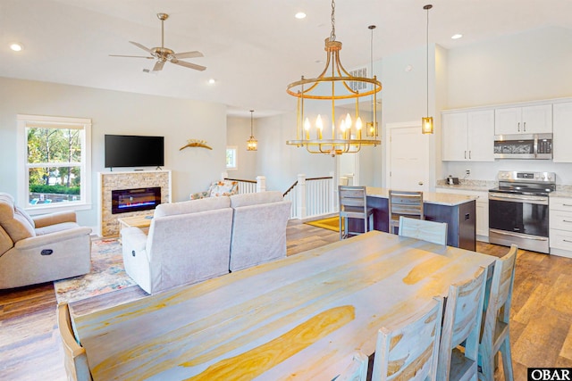 dining area with recessed lighting, a high ceiling, light wood-type flooring, a fireplace, and ceiling fan with notable chandelier