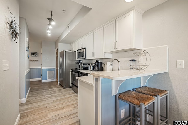 kitchen featuring a kitchen breakfast bar, stainless steel appliances, light countertops, wood finish floors, and white cabinetry