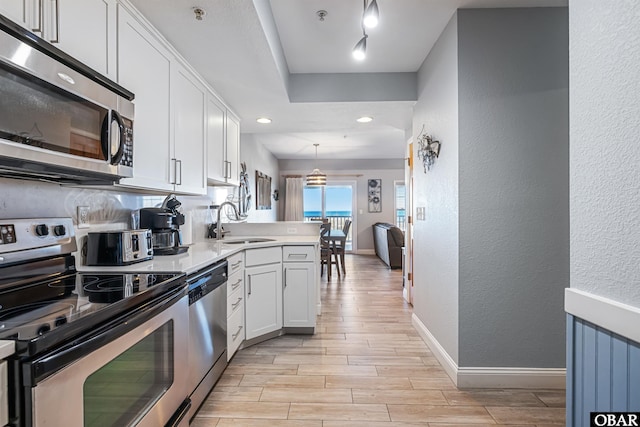 kitchen featuring stainless steel appliances, light countertops, white cabinetry, pendant lighting, and a sink