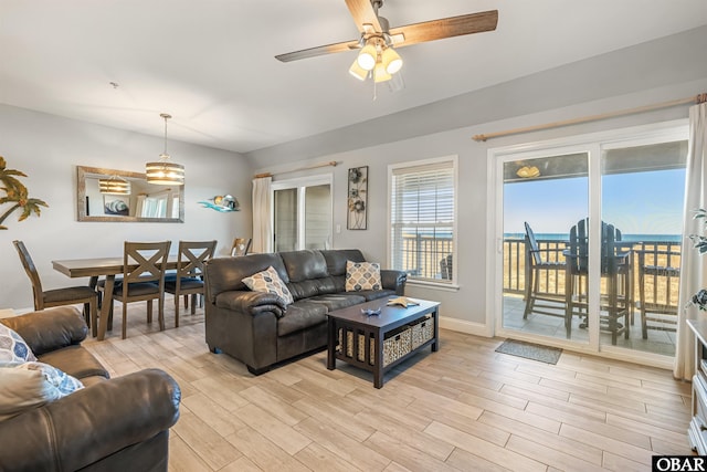 living room featuring a ceiling fan, baseboards, and light wood finished floors