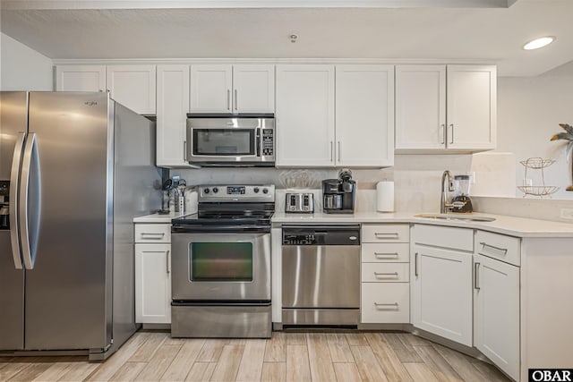 kitchen with appliances with stainless steel finishes, light countertops, wood finish floors, white cabinetry, and a sink