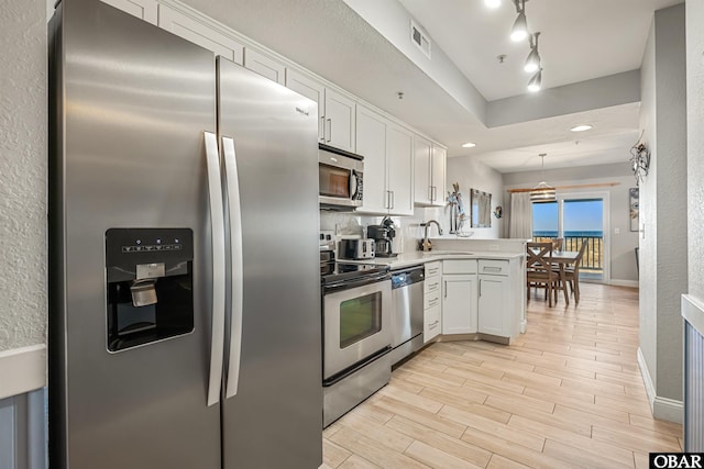 kitchen with stainless steel appliances, wood finish floors, white cabinets, light countertops, and decorative light fixtures