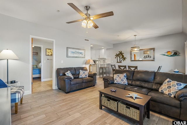 living area with light wood finished floors, ceiling fan, visible vents, and baseboards