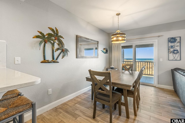 dining area with baseboards, a water view, and light wood finished floors