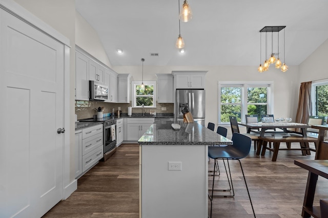 kitchen featuring a breakfast bar area, appliances with stainless steel finishes, a sink, vaulted ceiling, and a kitchen island