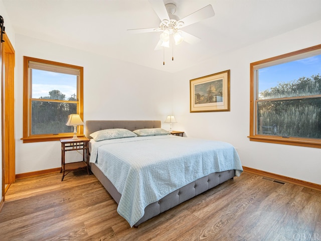 bedroom with baseboards, multiple windows, visible vents, and wood finished floors