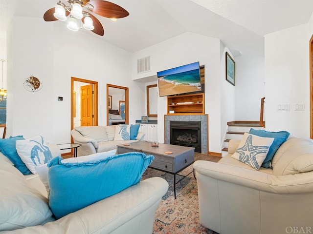 living room featuring high vaulted ceiling, ceiling fan, visible vents, and a tiled fireplace