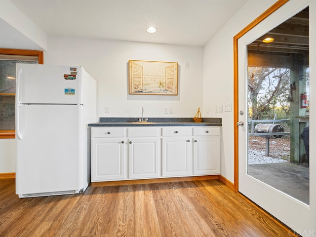 kitchen featuring light wood-style floors, dark countertops, freestanding refrigerator, and white cabinetry