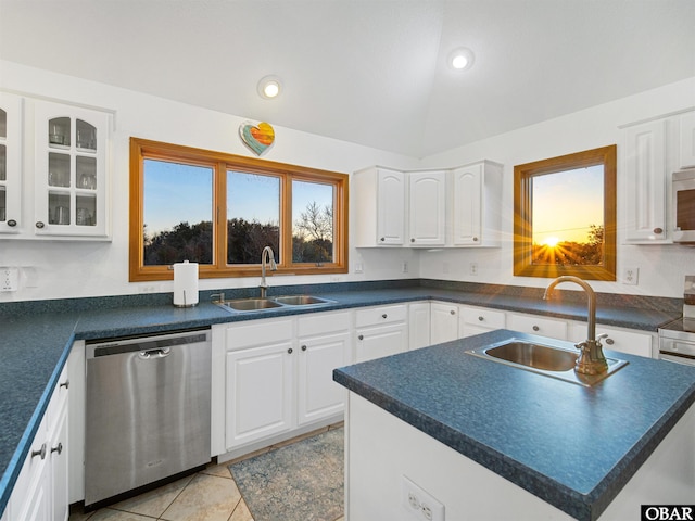 kitchen with a sink, white cabinetry, stainless steel dishwasher, dark countertops, and glass insert cabinets