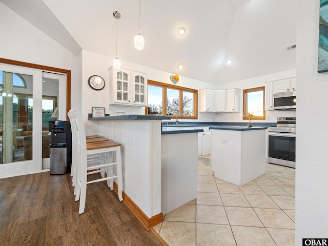 kitchen featuring stainless steel appliances, dark countertops, lofted ceiling, glass insert cabinets, and white cabinets