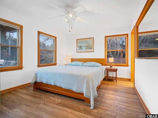 bedroom with a ceiling fan, multiple windows, baseboards, and wood finished floors