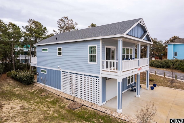 rear view of house with a shingled roof, board and batten siding, and a patio