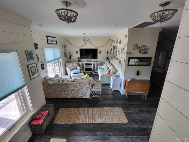 living area with a chandelier, vaulted ceiling, dark wood finished floors, and wooden walls