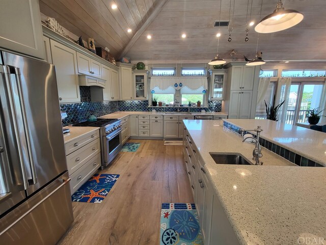 kitchen featuring premium appliances, glass insert cabinets, hanging light fixtures, and light stone counters