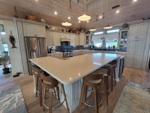 kitchen with visible vents, high quality appliances, hanging light fixtures, a large island, and glass insert cabinets