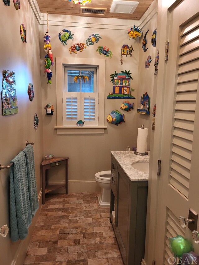 bathroom with brick floor, visible vents, toilet, vanity, and baseboards