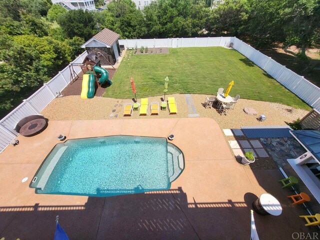 view of swimming pool featuring an outdoor fire pit, a lawn, a playground, and a fenced backyard