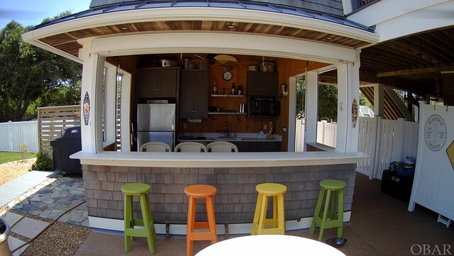 view of patio featuring outdoor dry bar, a sink, and fence