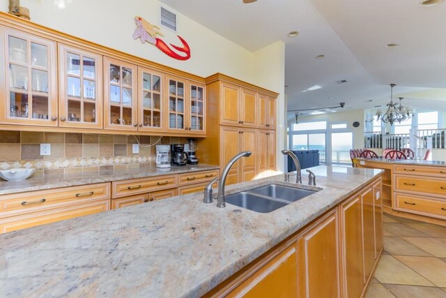 kitchen featuring visible vents, glass insert cabinets, a sink, and decorative light fixtures