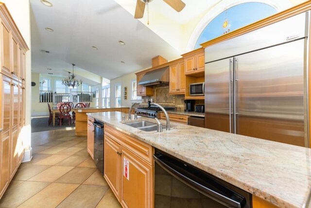 kitchen with stainless steel appliances, a kitchen island with sink, vaulted ceiling, a sink, and wall chimney exhaust hood