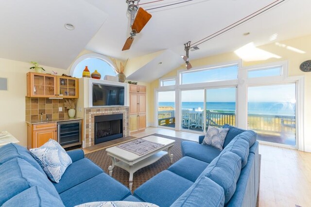 living room with lofted ceiling, visible vents, a brick fireplace, light wood-type flooring, and beverage cooler